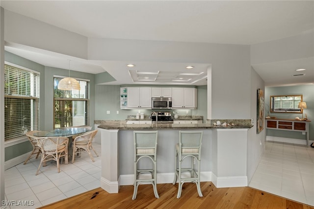 kitchen with kitchen peninsula, light tile patterned floors, stainless steel appliances, and white cabinetry