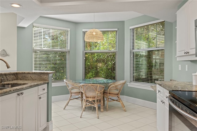 kitchen featuring light stone countertops, sink, decorative light fixtures, white cabinets, and plenty of natural light