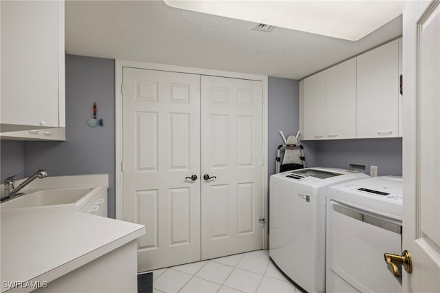 clothes washing area with cabinets, a textured ceiling, washer and clothes dryer, sink, and light tile patterned floors