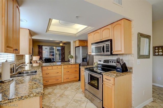 kitchen with sink, light brown cabinets, a tray ceiling, decorative backsplash, and appliances with stainless steel finishes