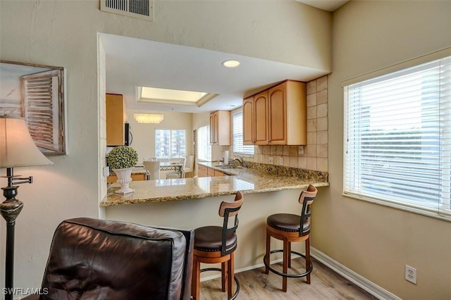 kitchen with a breakfast bar, backsplash, sink, light stone countertops, and kitchen peninsula