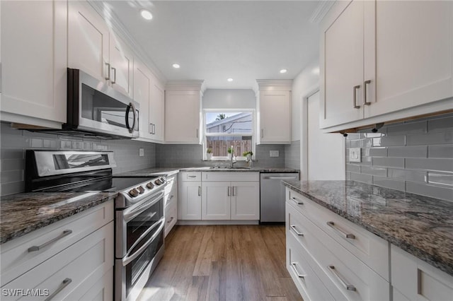 kitchen featuring stone countertops, white cabinets, appliances with stainless steel finishes, light wood-type flooring, and a sink