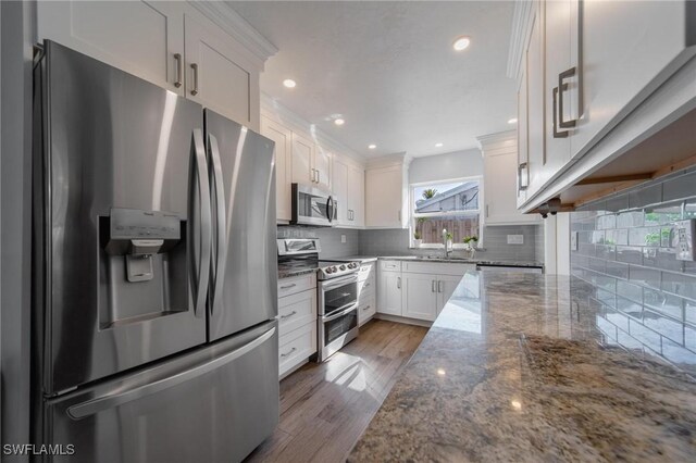 kitchen featuring decorative backsplash, white cabinetry, stainless steel appliances, and dark stone countertops