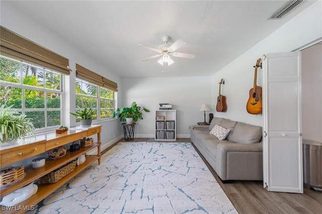 living room featuring light wood-style floors, visible vents, baseboards, and a ceiling fan