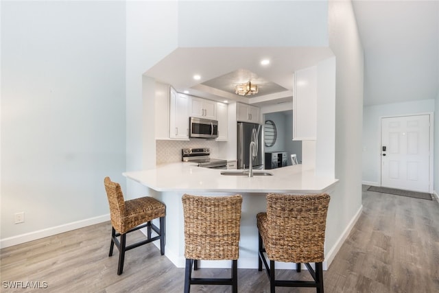 kitchen with sink, a breakfast bar area, appliances with stainless steel finishes, white cabinetry, and kitchen peninsula