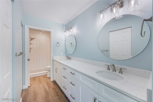 bathroom with hardwood / wood-style flooring, vanity, a tile shower, and toilet