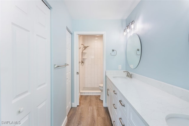 bathroom featuring wood-type flooring, toilet, vanity, and a tile shower