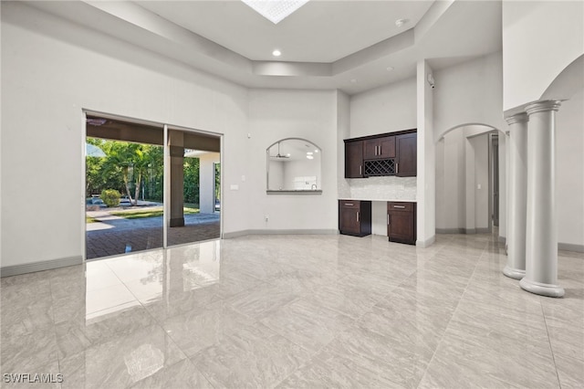 unfurnished living room featuring ornate columns and a towering ceiling