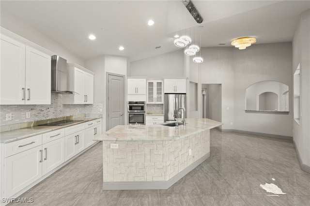 kitchen with a large island with sink, white cabinets, stainless steel appliances, and wall chimney range hood