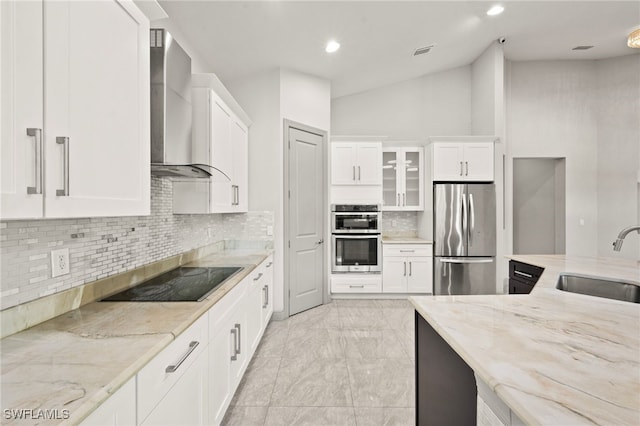 kitchen with appliances with stainless steel finishes, light stone counters, sink, wall chimney range hood, and white cabinets