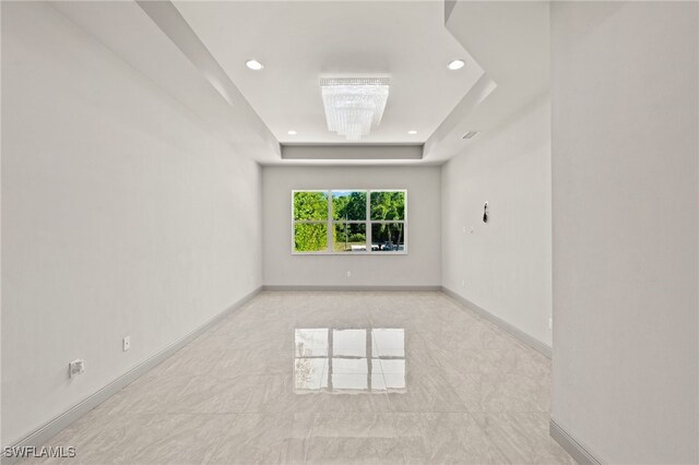 unfurnished room featuring a raised ceiling and a chandelier