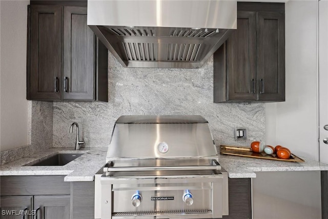 kitchen with wall chimney range hood, light stone counters, decorative backsplash, and sink