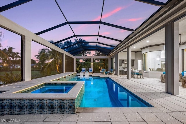 pool at dusk with glass enclosure, an in ground hot tub, and a patio area