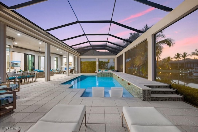 pool at dusk with an in ground hot tub, a patio area, a water view, ceiling fan, and a lanai