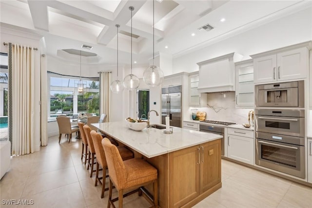 kitchen with white cabinetry, beam ceiling, a kitchen island with sink, coffered ceiling, and stainless steel appliances