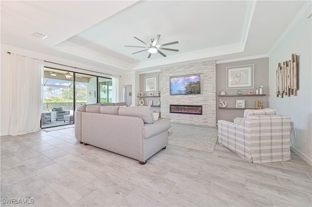 living room with a raised ceiling, ornamental molding, a stone fireplace, and ceiling fan