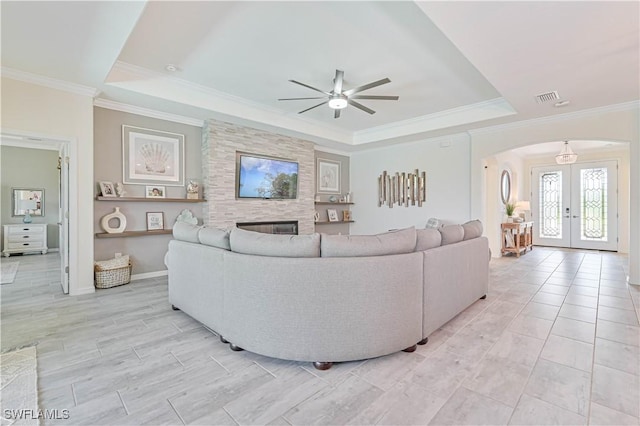 living room with ceiling fan, a tray ceiling, a fireplace, ornamental molding, and french doors