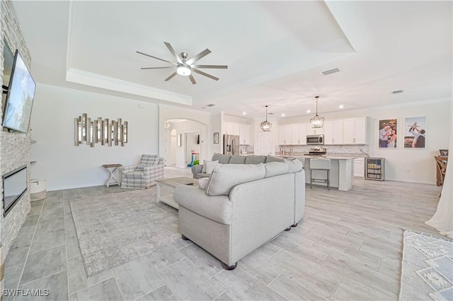 living room featuring a fireplace, ornamental molding, a raised ceiling, and ceiling fan