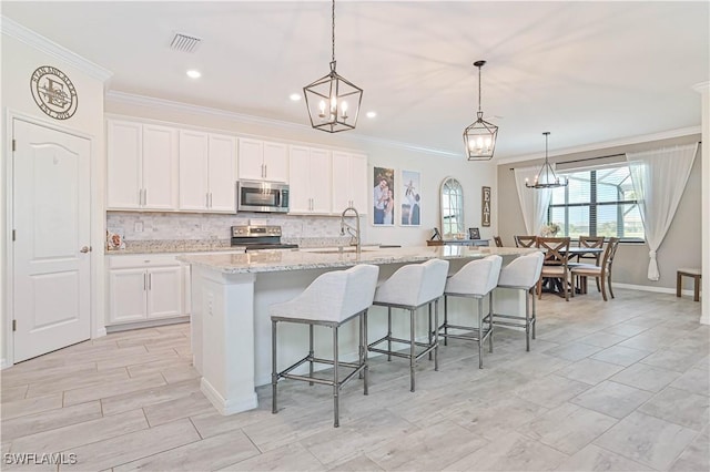 kitchen with stainless steel appliances, decorative light fixtures, a kitchen island with sink, and white cabinets