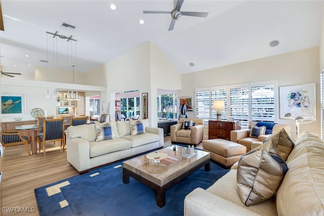 living room with ceiling fan with notable chandelier, light wood-type flooring, and high vaulted ceiling