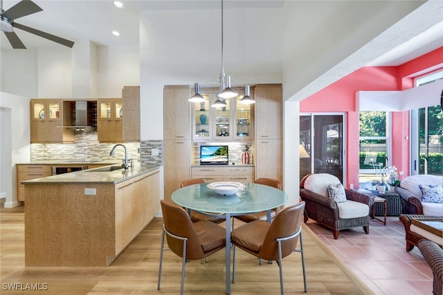 kitchen featuring pendant lighting, ceiling fan with notable chandelier, wall chimney range hood, sink, and kitchen peninsula