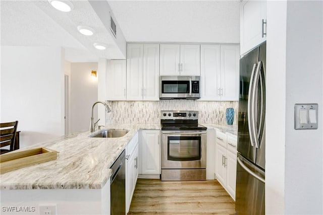 kitchen with kitchen peninsula, appliances with stainless steel finishes, light stone counters, sink, and white cabinets