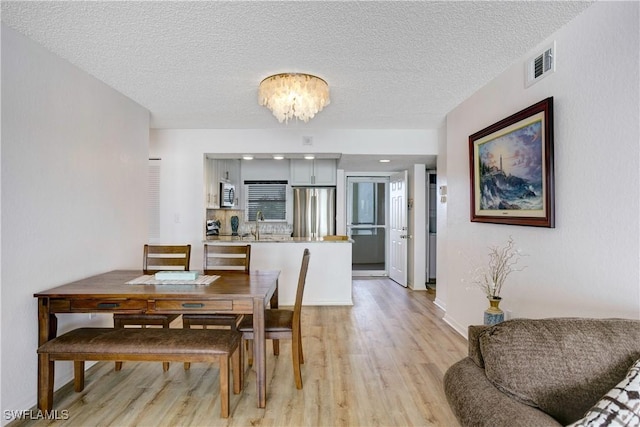 dining area with light hardwood / wood-style floors, a textured ceiling, and an inviting chandelier