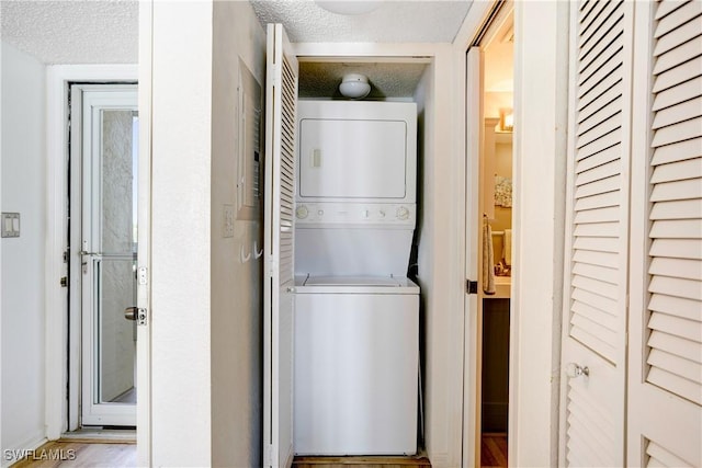 clothes washing area with stacked washer / drying machine and a textured ceiling