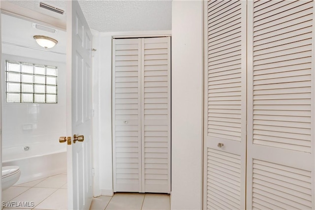 bathroom with tile patterned floors, toilet, a textured ceiling, and bathtub / shower combination