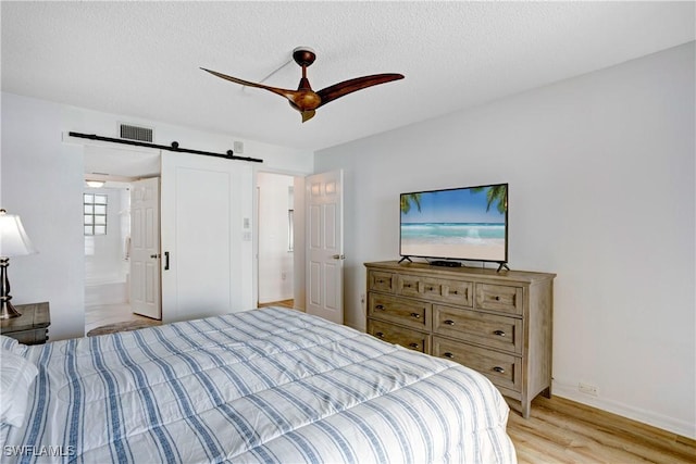 bedroom featuring ensuite bathroom, ceiling fan, a barn door, light wood-type flooring, and a textured ceiling