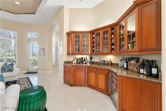 bar with sink, stone countertops, light tile patterned floors, and a raised ceiling