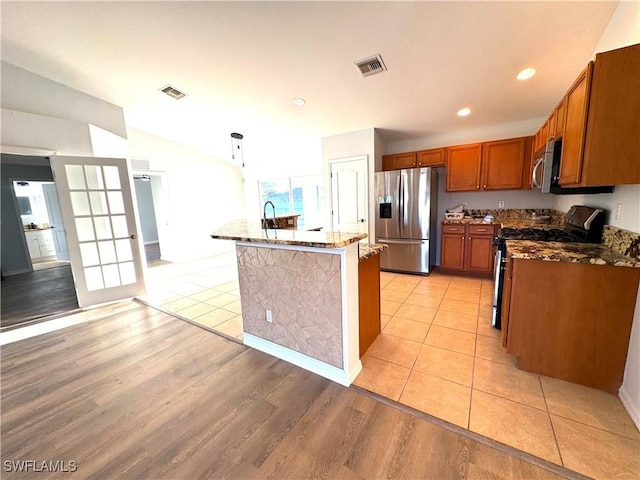 kitchen featuring light stone counters, stainless steel appliances, a center island with sink, light hardwood / wood-style floors, and hanging light fixtures