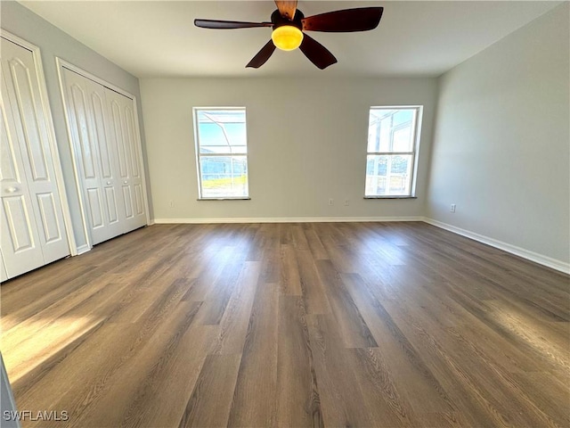 unfurnished bedroom with multiple windows, two closets, ceiling fan, and dark wood-type flooring