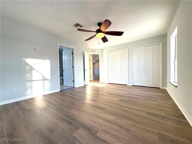 unfurnished bedroom with connected bathroom, multiple closets, ceiling fan, and dark wood-type flooring