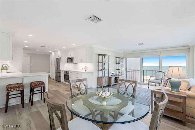 dining space with sink, a water view, crown molding, and light hardwood / wood-style flooring