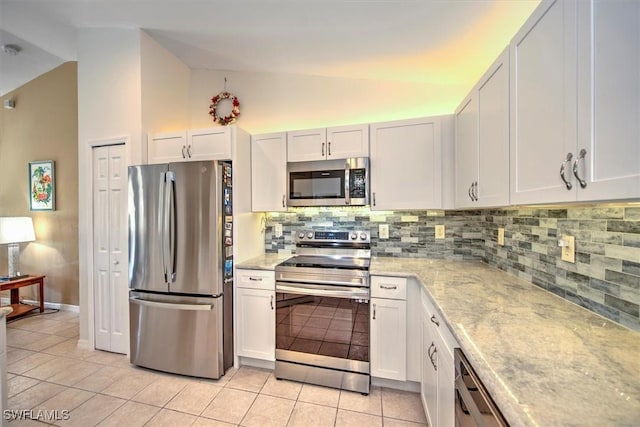 kitchen featuring backsplash, stainless steel appliances, white cabinetry, lofted ceiling, and light tile patterned flooring