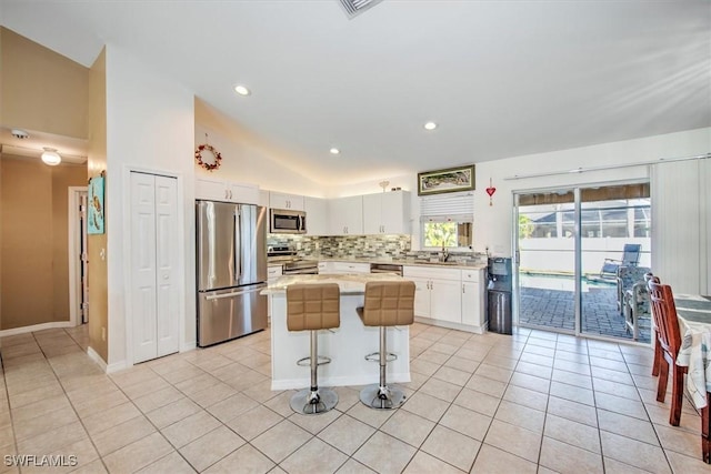 kitchen with white cabinetry, a center island, vaulted ceiling, a breakfast bar area, and appliances with stainless steel finishes