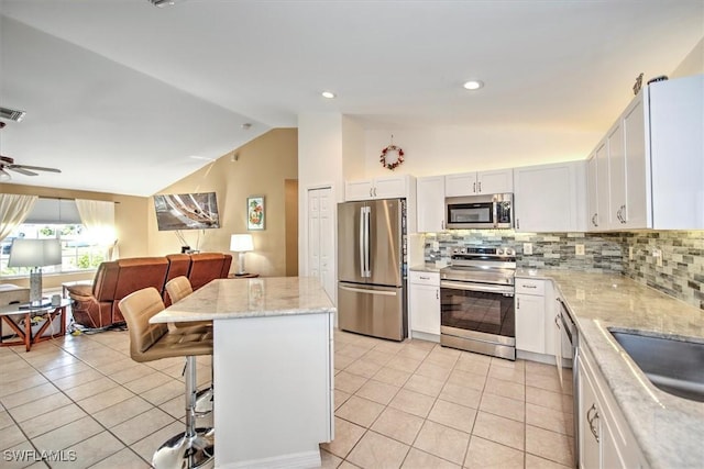 kitchen with backsplash, vaulted ceiling, appliances with stainless steel finishes, a kitchen island, and white cabinetry