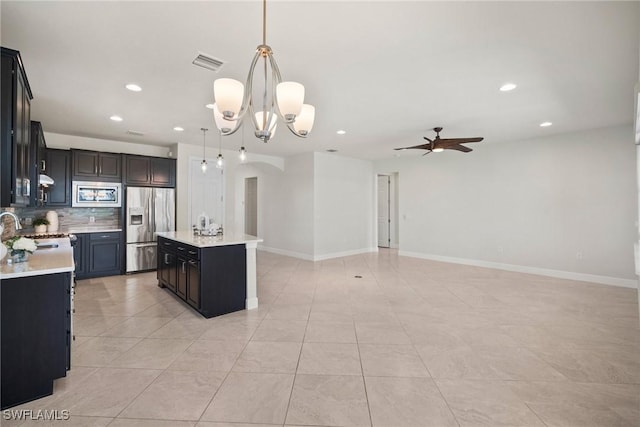 kitchen featuring a center island, stainless steel appliances, backsplash, pendant lighting, and ceiling fan with notable chandelier