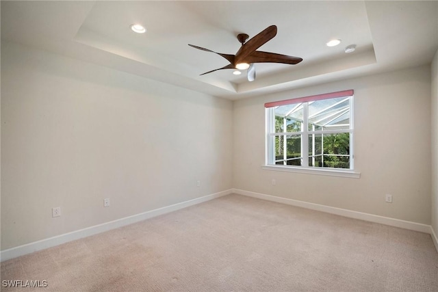 empty room featuring light carpet, a tray ceiling, and ceiling fan