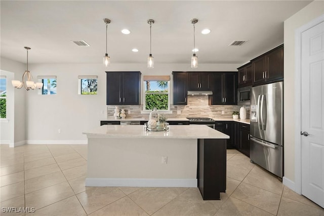 kitchen with a center island, hanging light fixtures, light tile patterned floors, light stone countertops, and stainless steel appliances