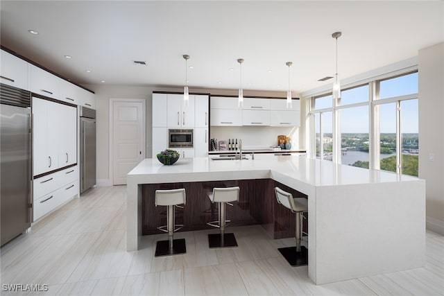 kitchen with white cabinets, a kitchen breakfast bar, a spacious island, built in appliances, and decorative light fixtures