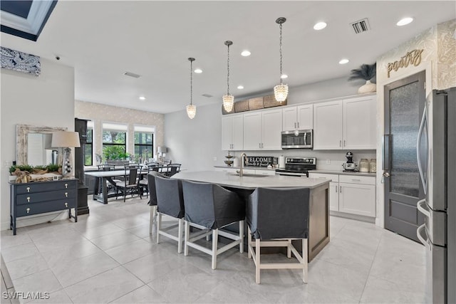 kitchen featuring white cabinetry, stainless steel appliances, sink, hanging light fixtures, and a center island with sink