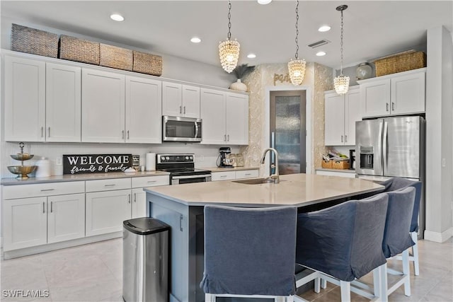 kitchen with white cabinetry, stainless steel appliances, sink, hanging light fixtures, and a center island with sink