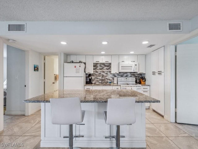 kitchen with white cabinets, light stone countertops, a kitchen bar, and white appliances