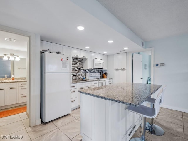 kitchen featuring a breakfast bar, white appliances, white cabinets, sink, and light stone counters