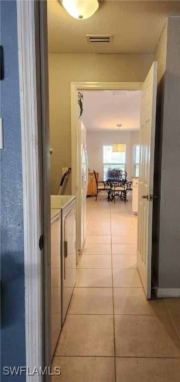 hallway with separate washer and dryer and light tile patterned floors