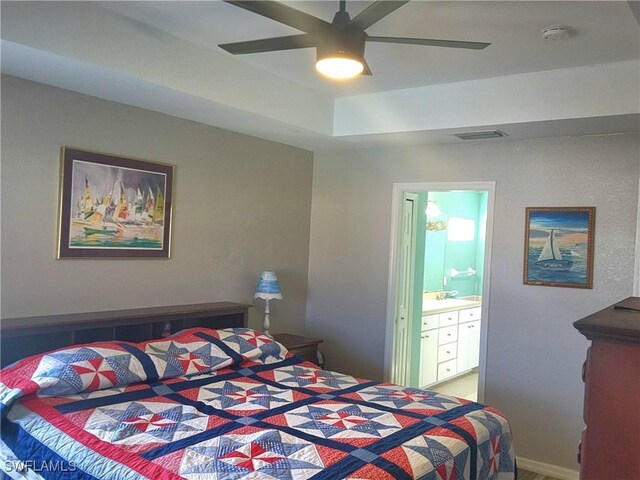 bedroom with ceiling fan, ensuite bathroom, and a tray ceiling