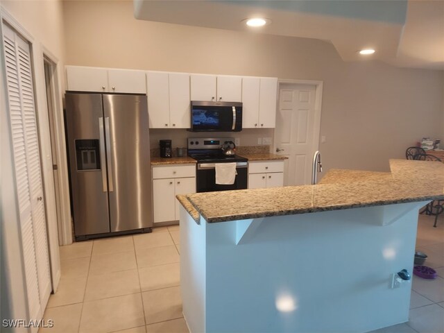 kitchen featuring light tile patterned flooring, a breakfast bar, white cabinetry, an island with sink, and stainless steel appliances