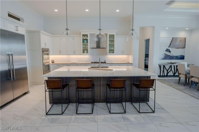 kitchen with pendant lighting, a kitchen island with sink, white cabinets, a kitchen breakfast bar, and appliances with stainless steel finishes